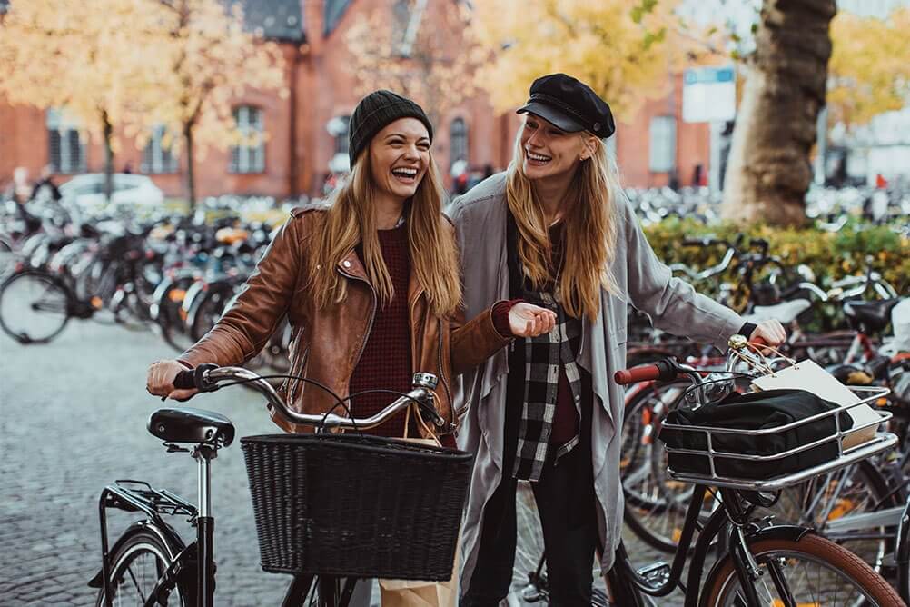 Two unga kvinnor leder sina cyklar genom staden nöjda med att minska sitt koldioxidutsläpp