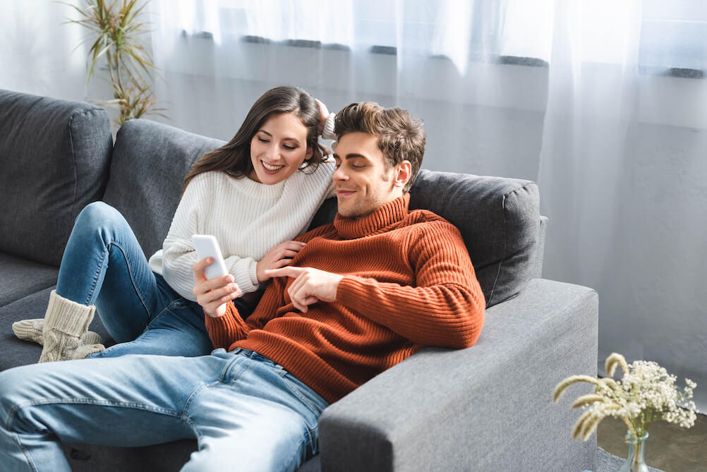 A couple on a sofa, enjoying Live Casino Game Shows on their phone.